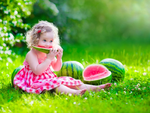 petite fille assise dans son jardin mange de la pastèque